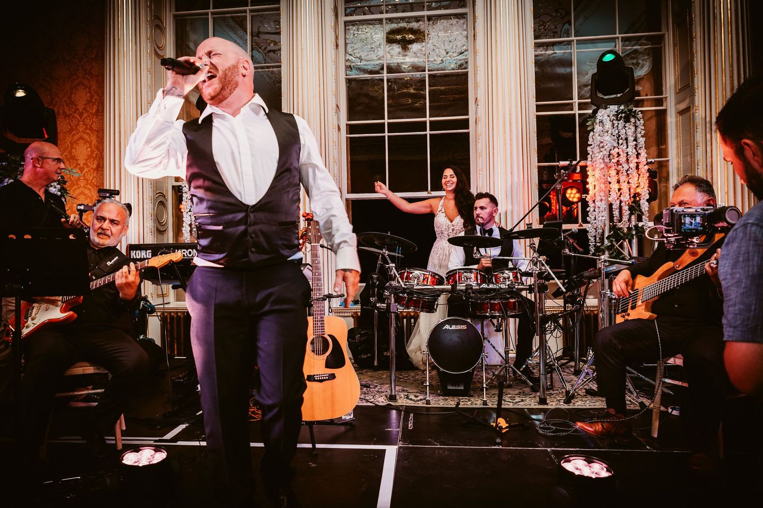 Live band performs at an elegant wedding reception with instruments and equipment on stage.