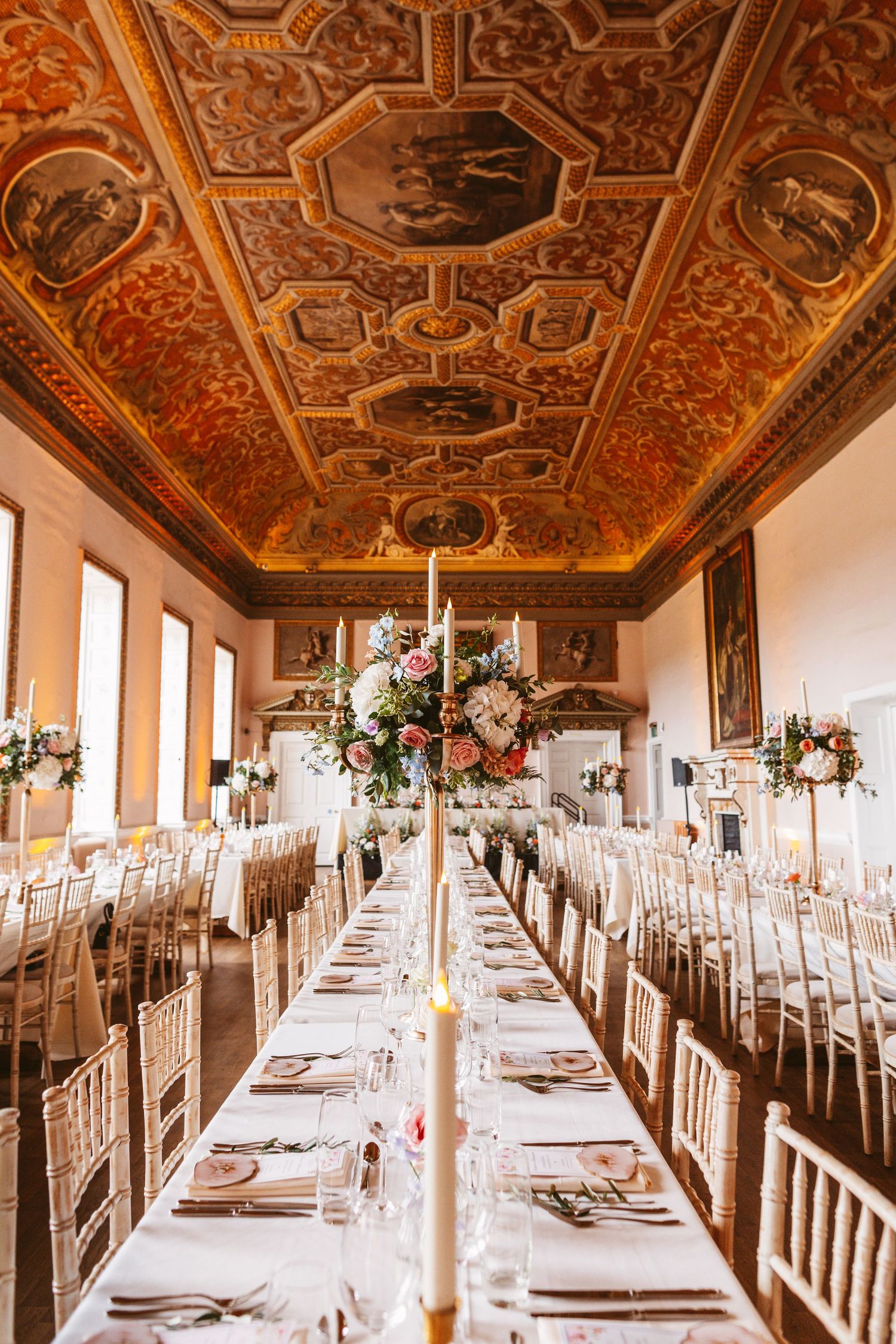 Wedding reception hall with ornate Renaissance ceiling and long tables set for dinner.