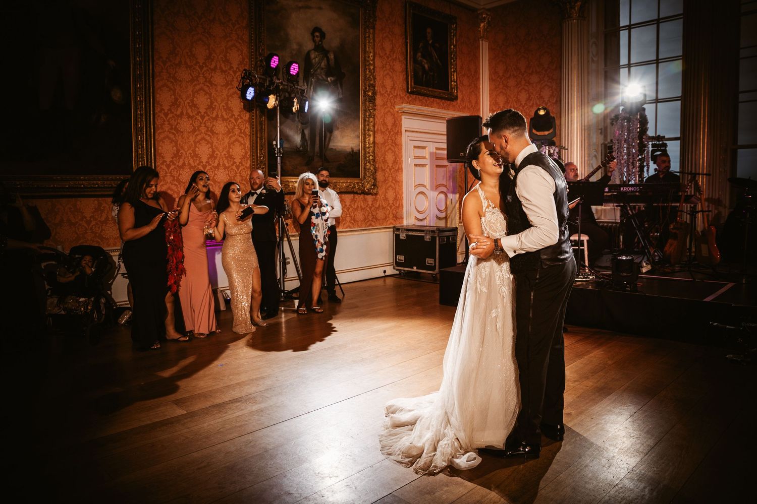 Romantic first dance moment in historic ballroom with guests watching from the sidelines.