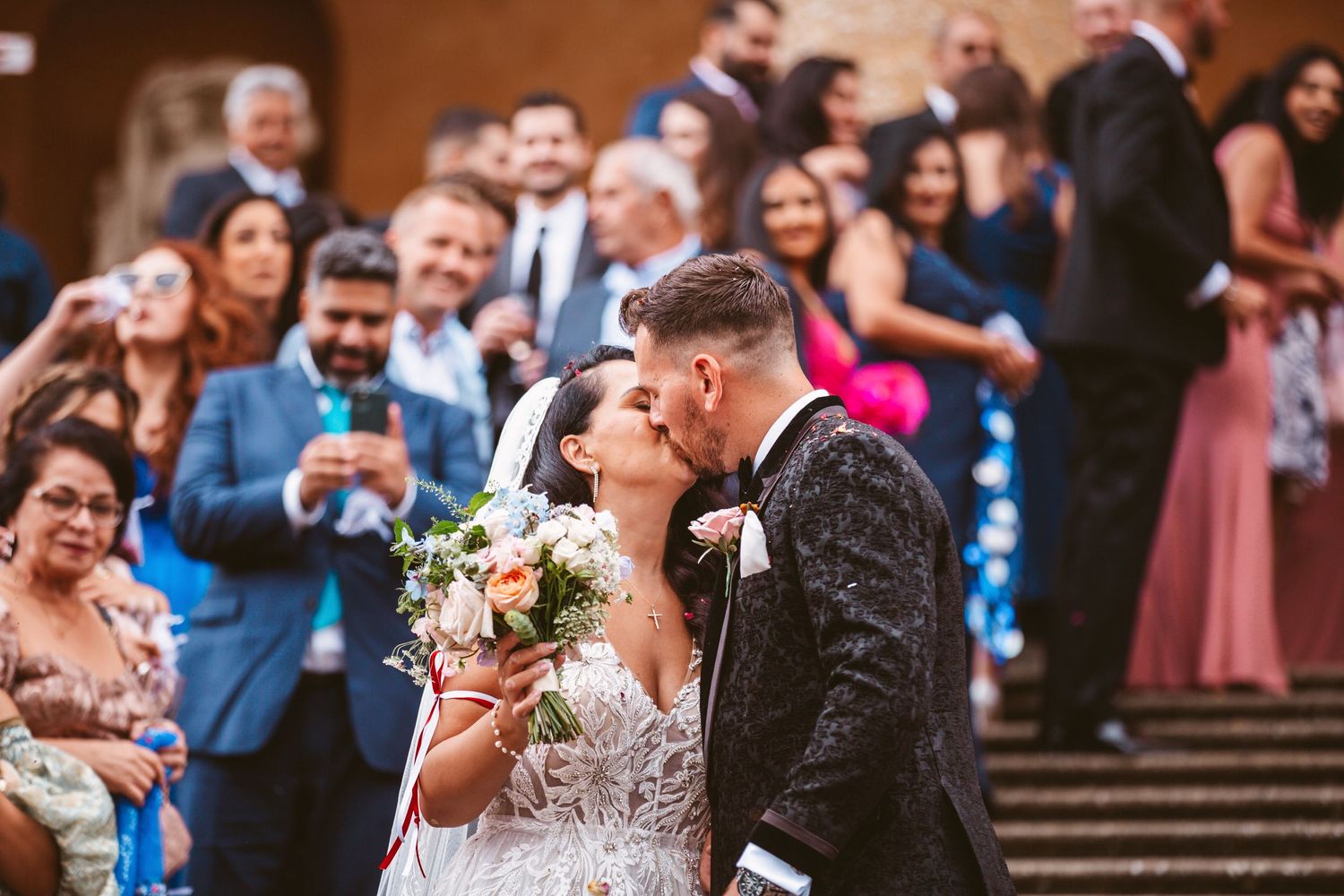 Romantic wedding moment captured on stone steps with celebrating guests.