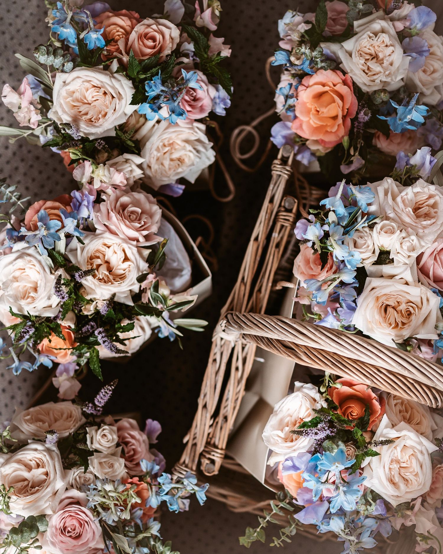 Beautiful floral arrangement of pink roses and blue flowers in a wicker basket.
