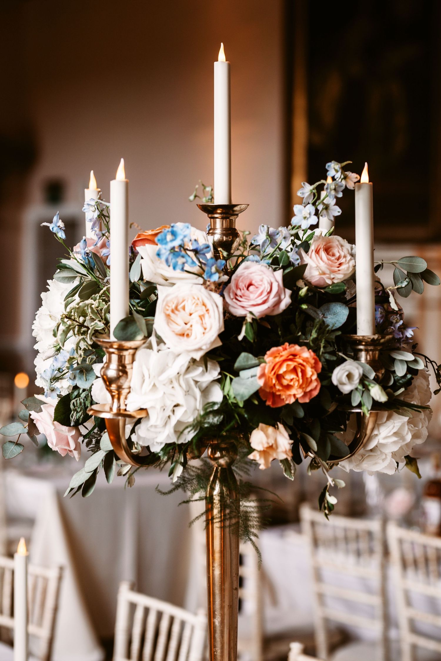 Elegant floral centerpiece with pink roses and white candles in gold candelabra.