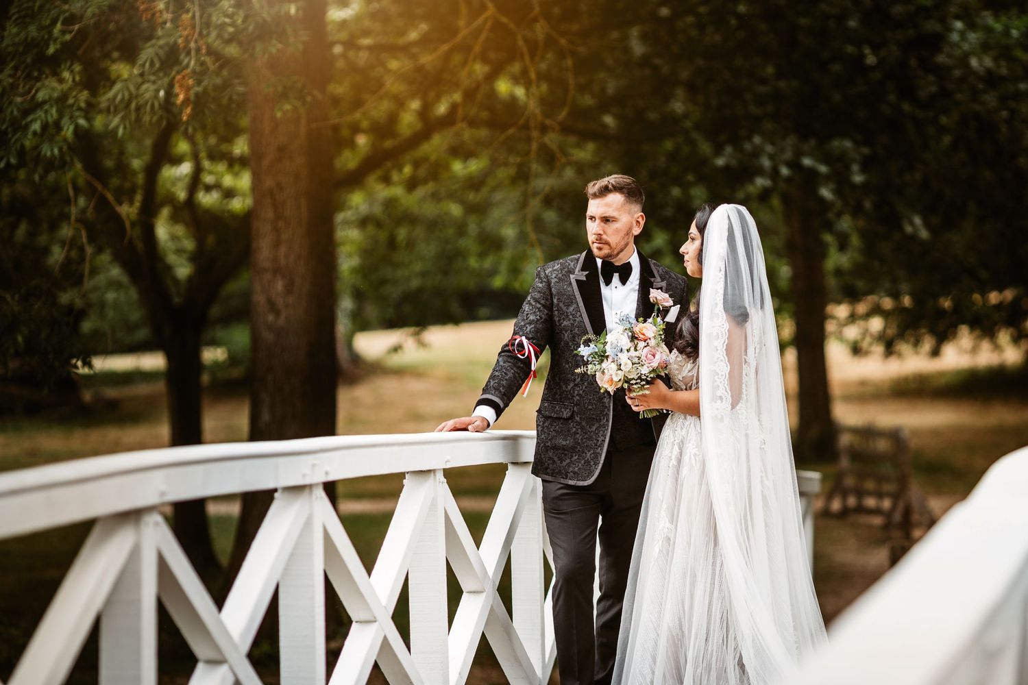 Romantic moment captured on a white wooden bridge in a sunlit garden setting.