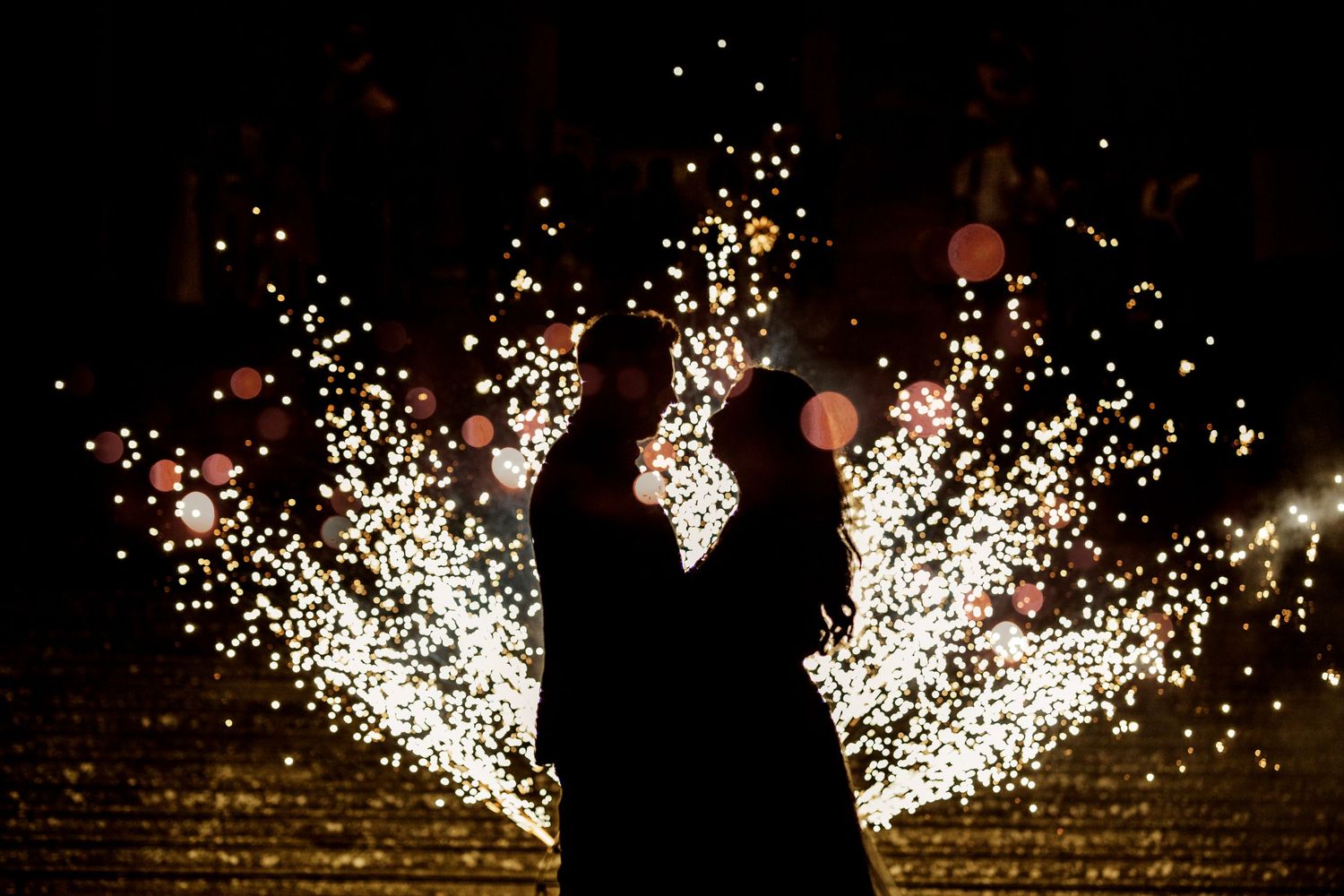 Silhouetted figures stand before cascading white sparkler fountains creating a magical moment.