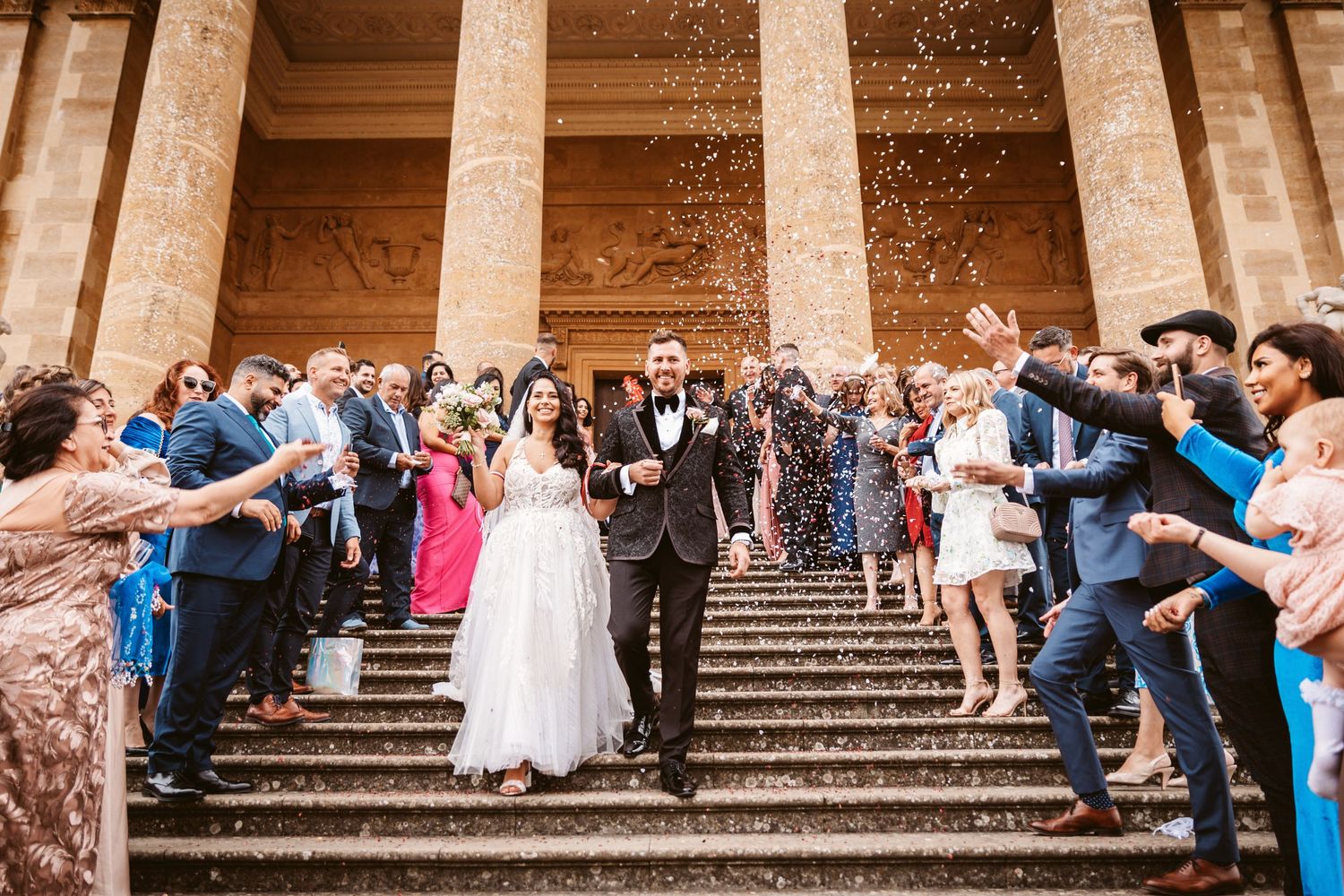 Celebratory moment as wedding party exits while guests throw confetti on historic building steps.