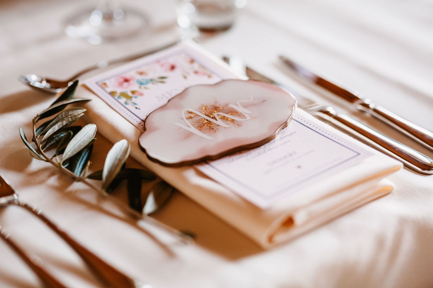 Close-up of wedding place setting with floral menu card and rose gold details.