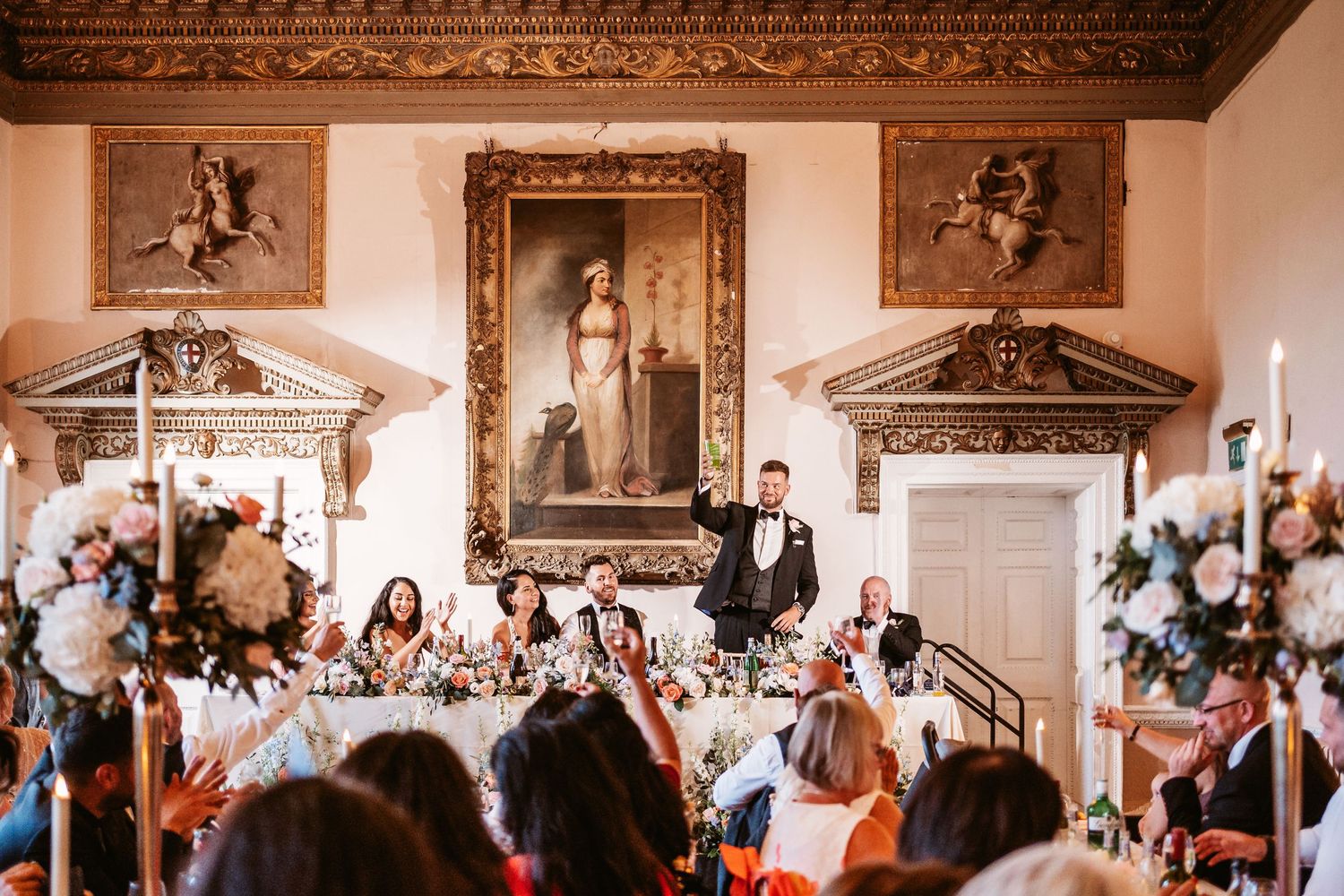 Elegant wedding reception hall with classical artwork and floral arrangements during speeches.
