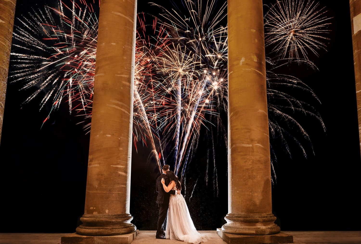 Stunning fireworks display illuminates a couple framed between elegant stone columns during a celebration.