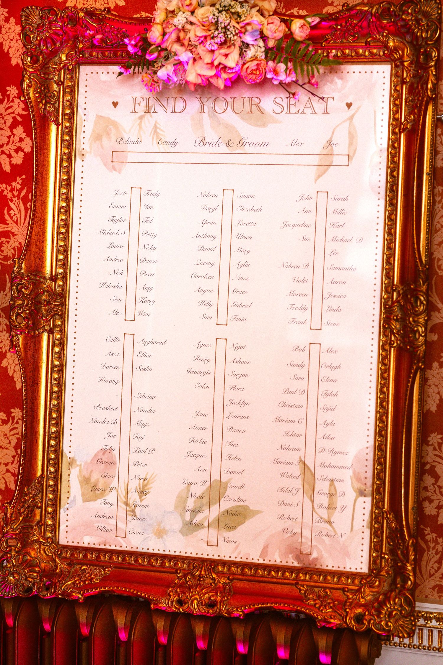 Wedding seating chart displayed in ornate gold frame with floral design details.