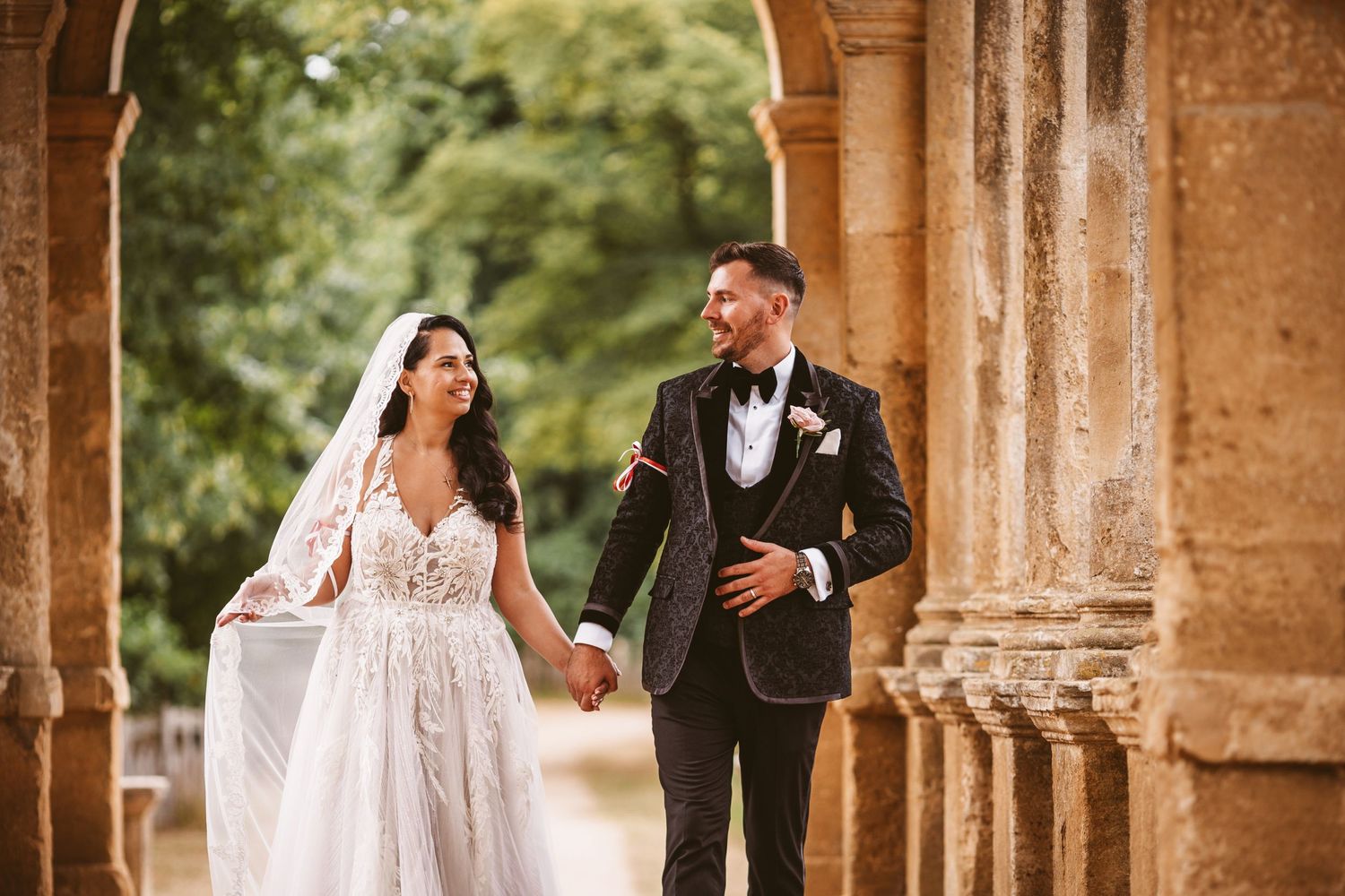 Couple shares romantic moment walking through classical stone archway.