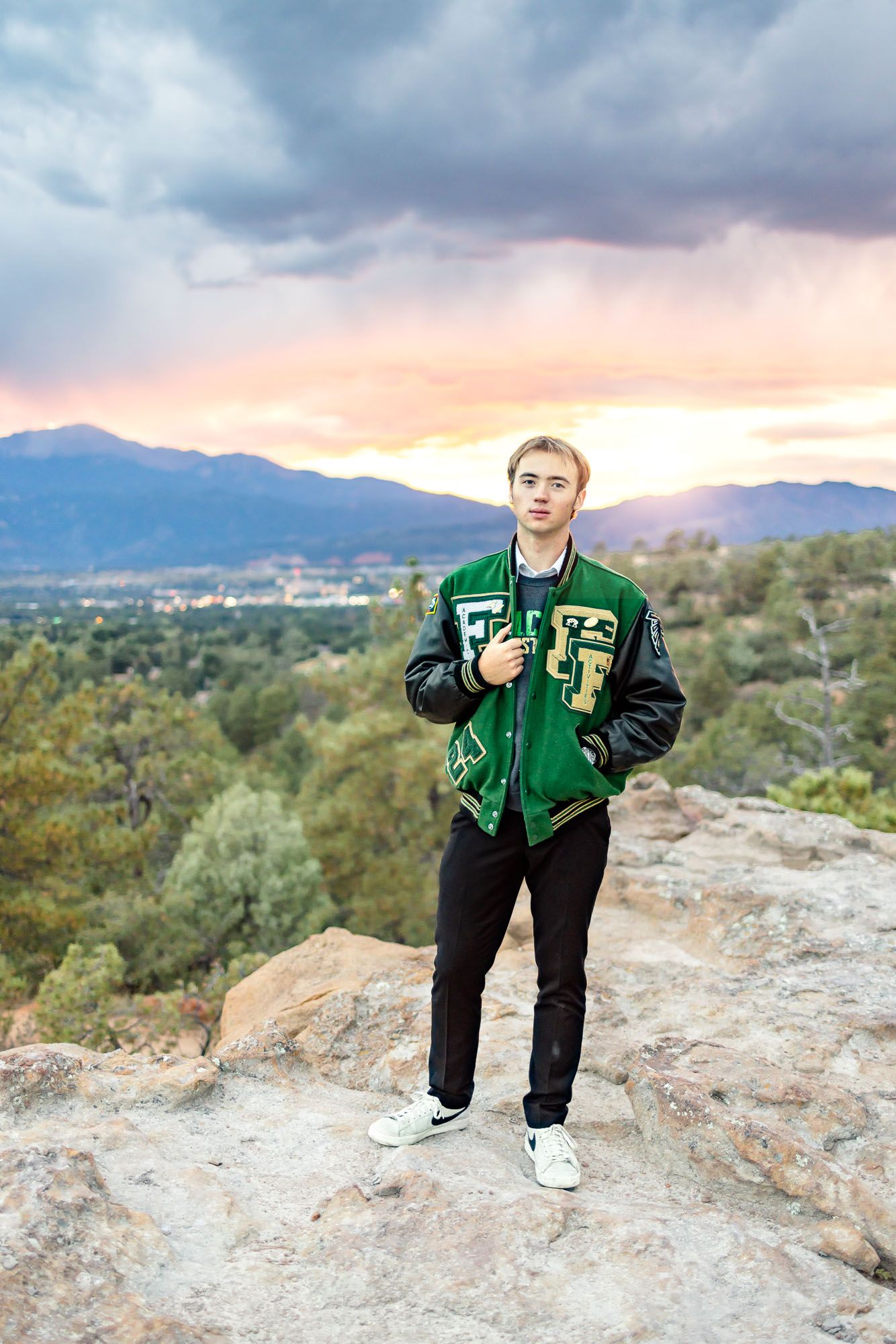 Senior guy poses in letterman jacket at sunset at his senior session at Palmer Park in Colorado Springs.