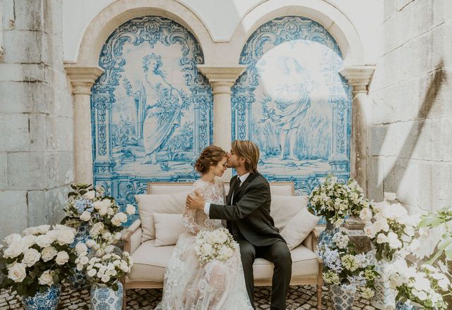 Wedding couple seated against blue and white tiled wall with floral arrangements.