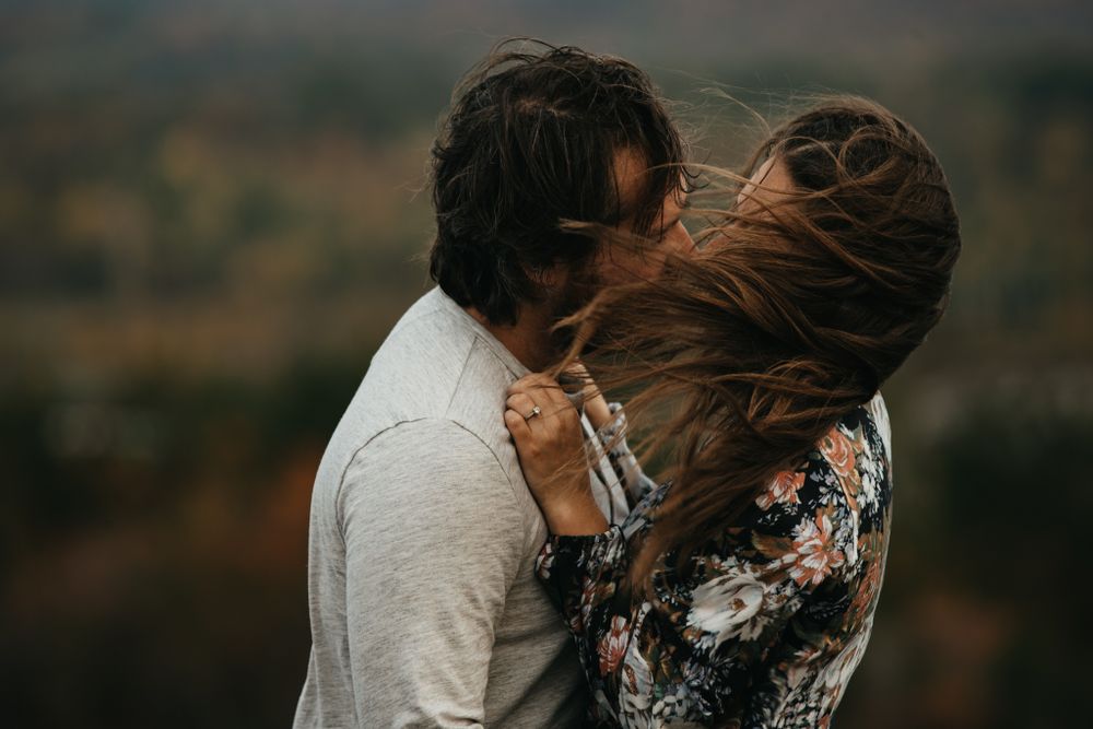 Candid romantic moment between couple with wind-blown hair on hilltop.