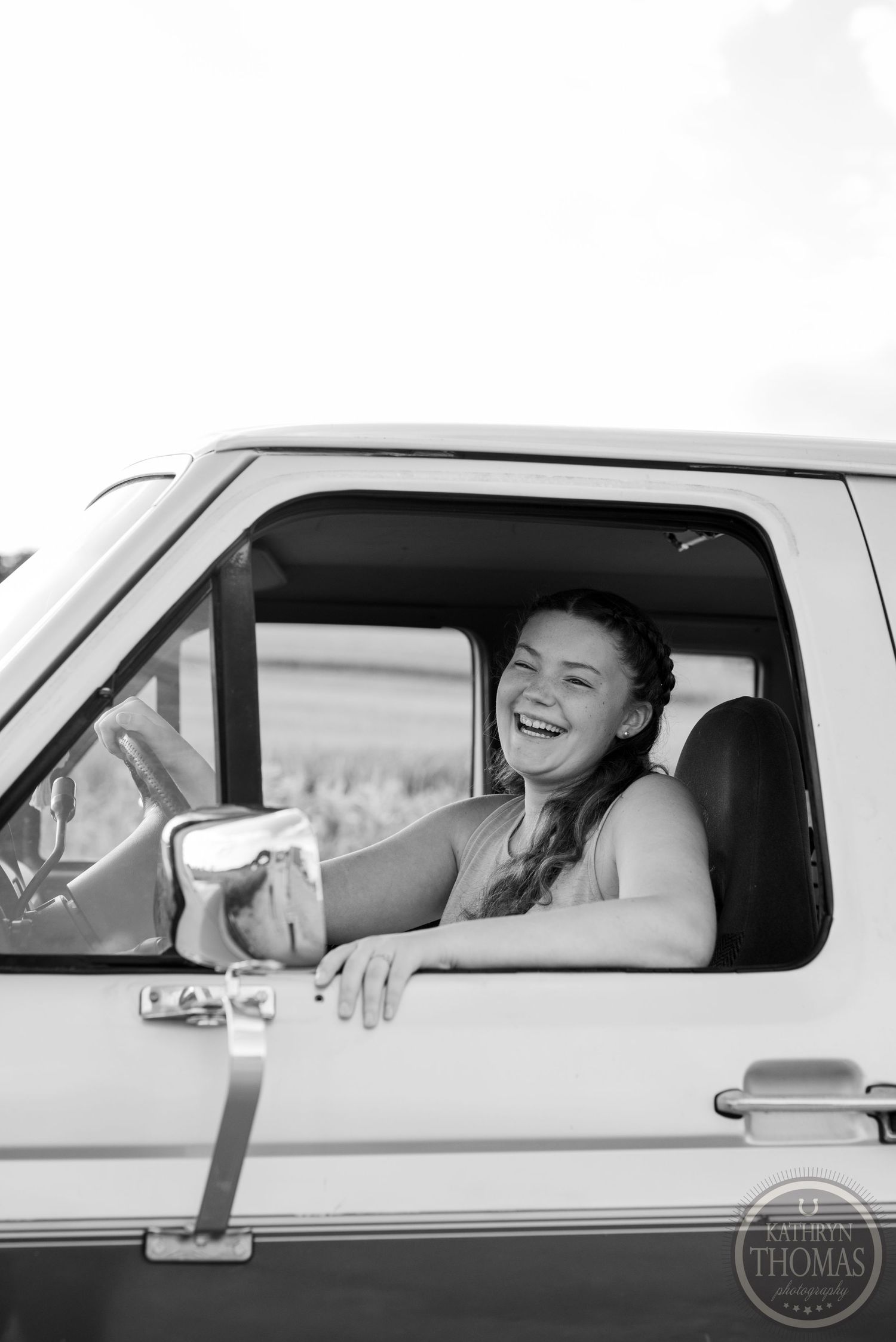 Black and white photo capturing someone through driver's window of classic pickup truck.