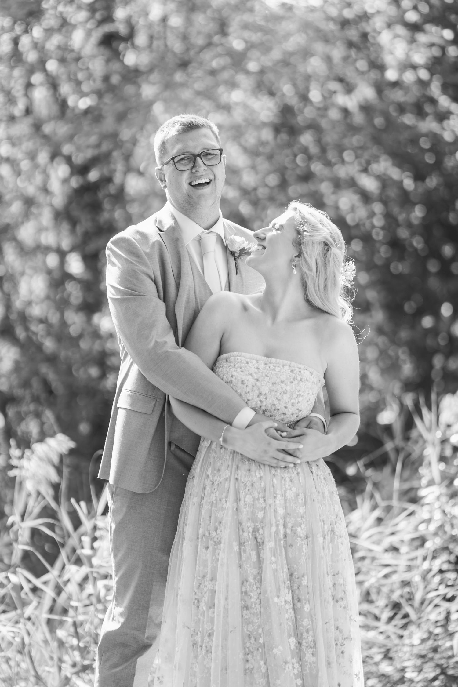 Image of bride and groom laughing in front of outdoor shrubbery