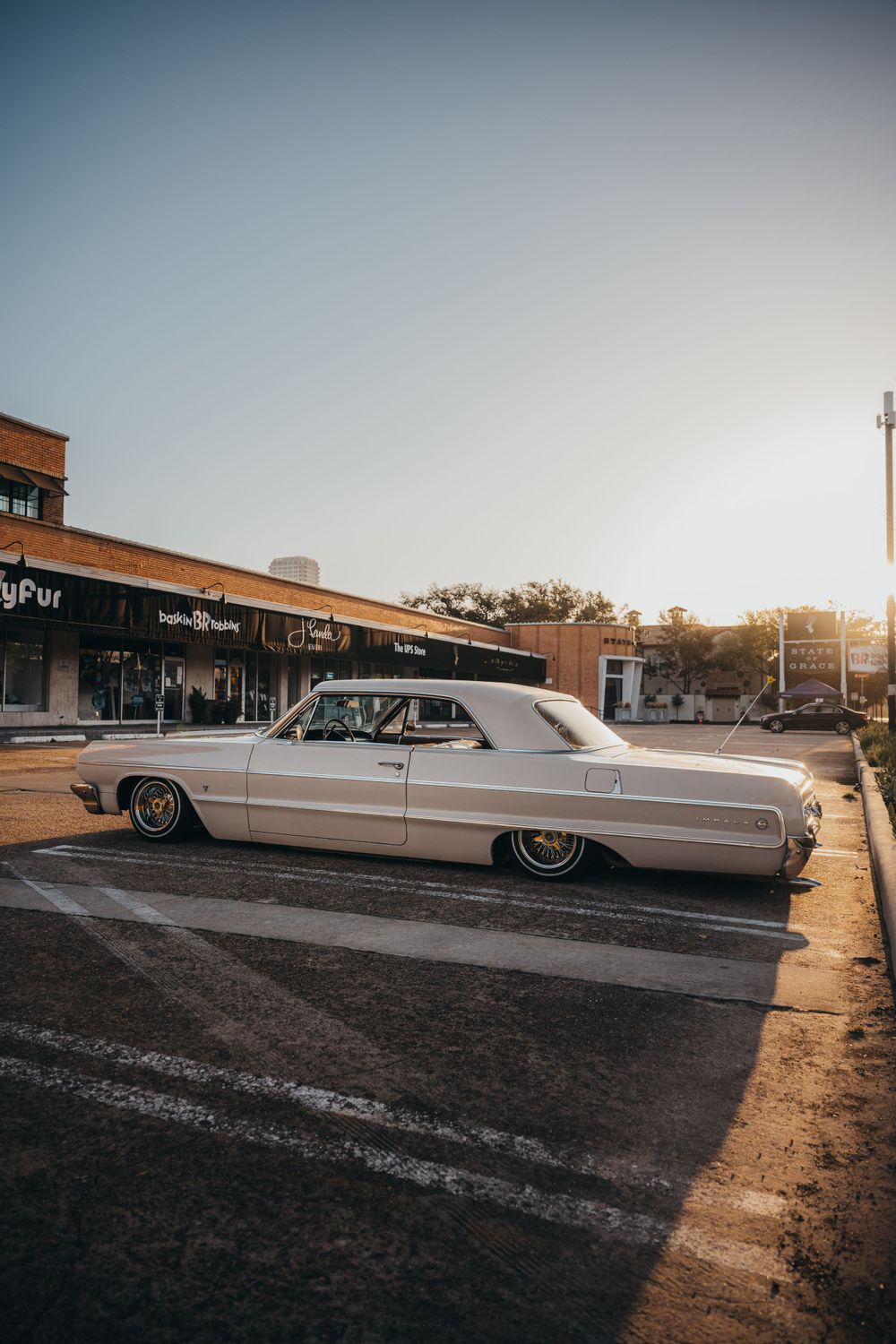 Classic white Cadillac lowrider parked outside a strip mall at sunset.
