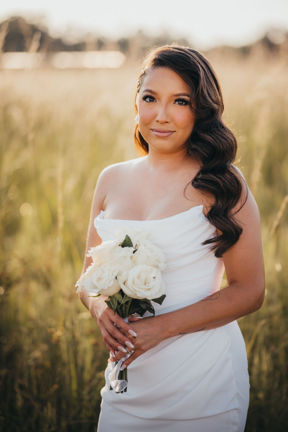 Bride in white dress holds white roses during outdoor portrait session in natural lighting.