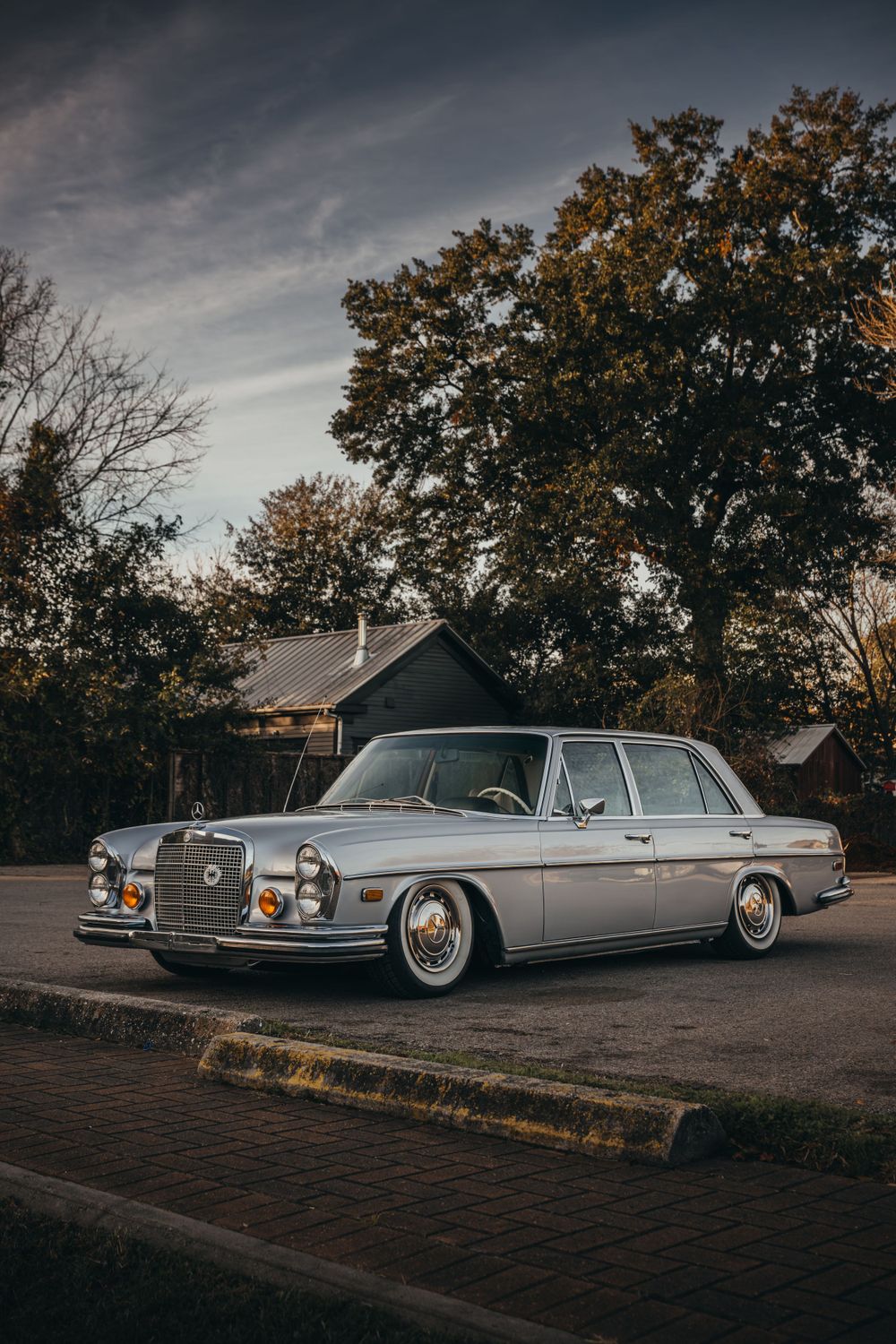 Classic silver Mercedes-Benz luxury car parked on street at dusk.