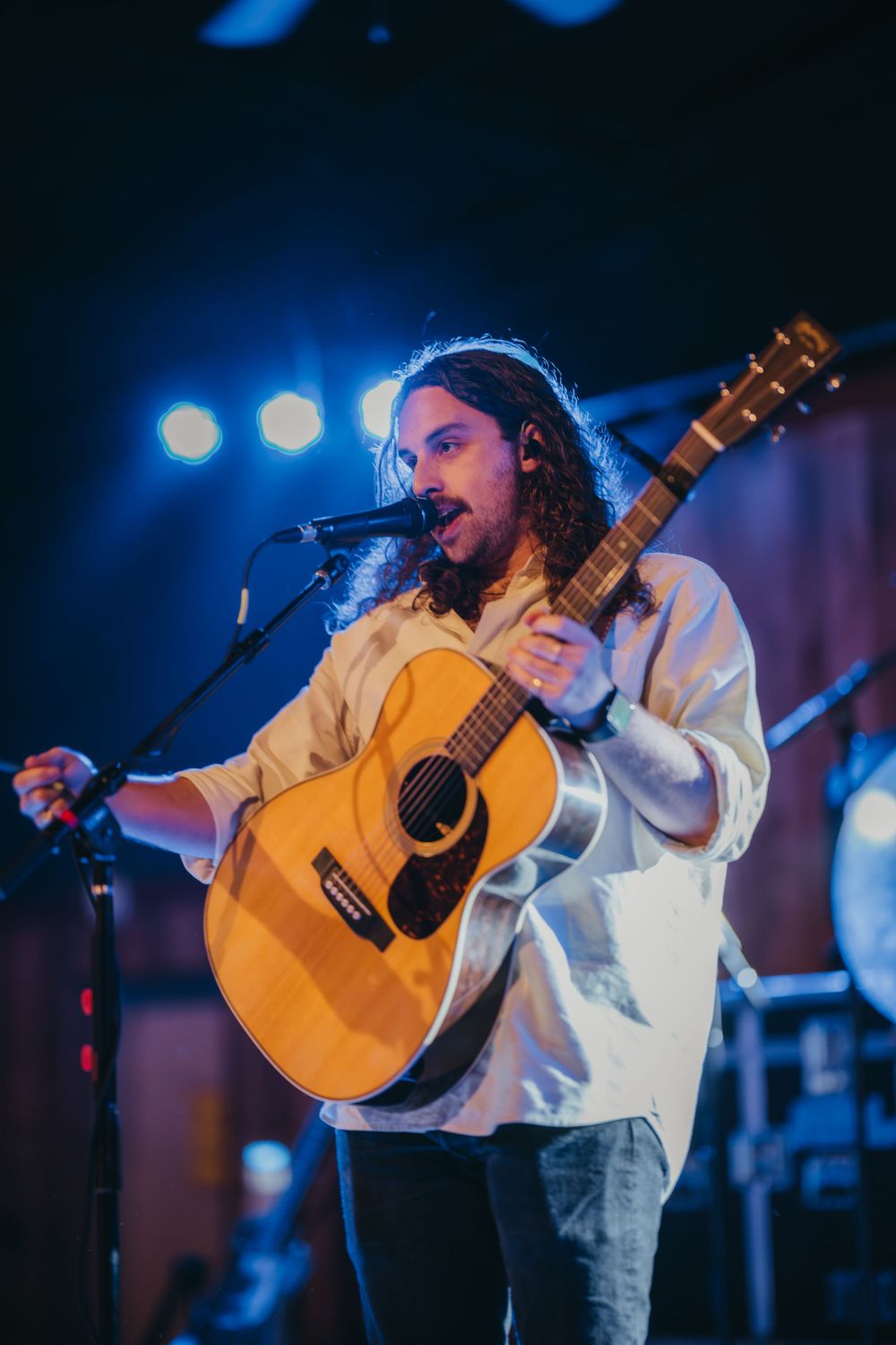 Concert performance with musician playing acoustic guitar under blue stage lighting.