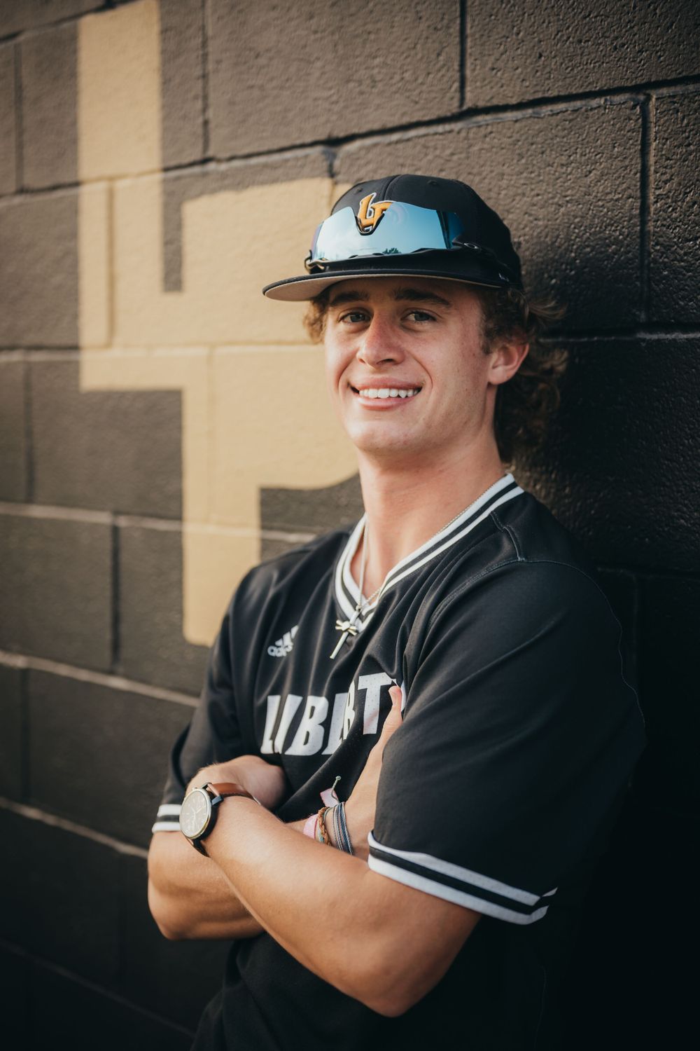 Baseball player in uniform poses against brick wall for sports portrait.