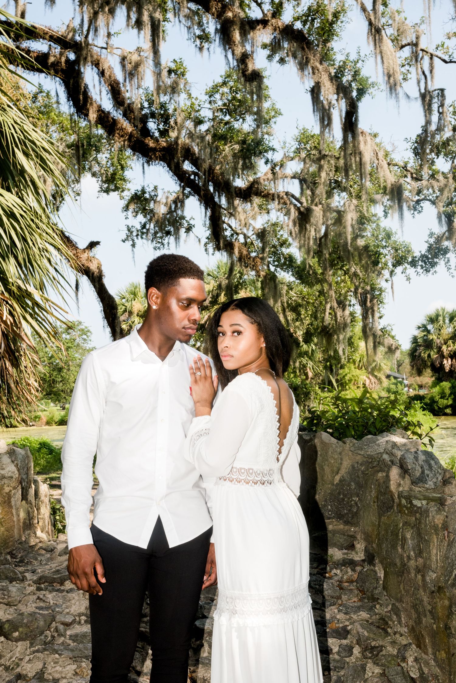 Elegant engagement photo of couple in white against natural backdrop with Spanish moss.