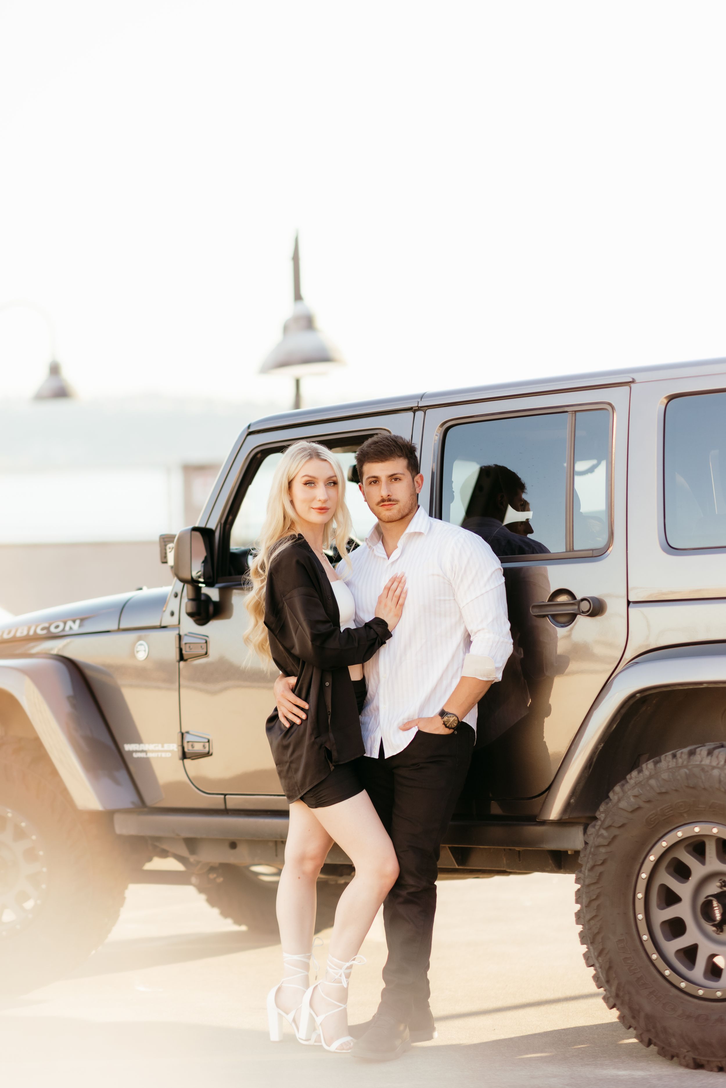 A couple in casual attire poses against their Jeep Wrangler during a sunny afternoon.