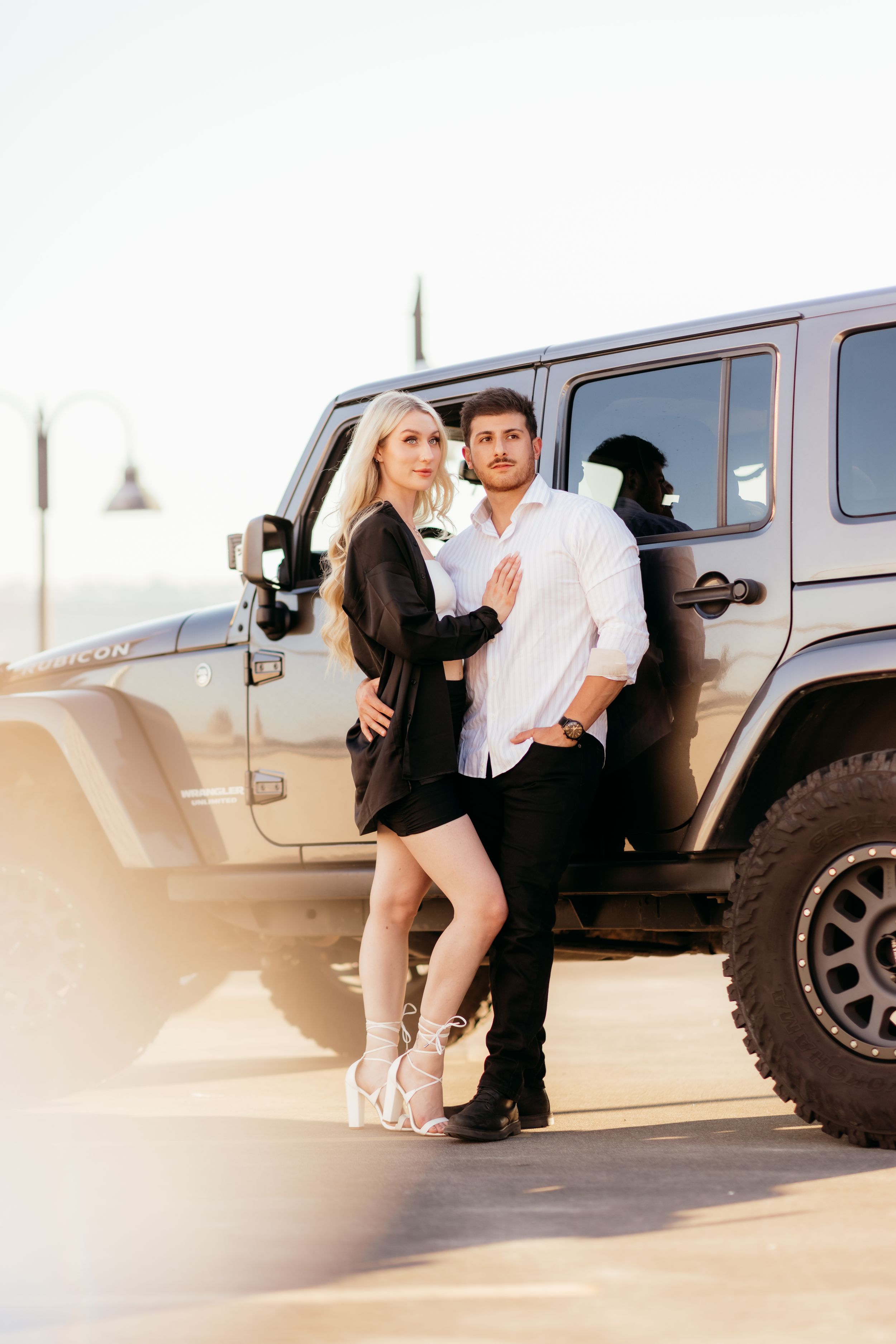 A stylish couple poses against a Jeep Wrangler during a sunset photoshoot.