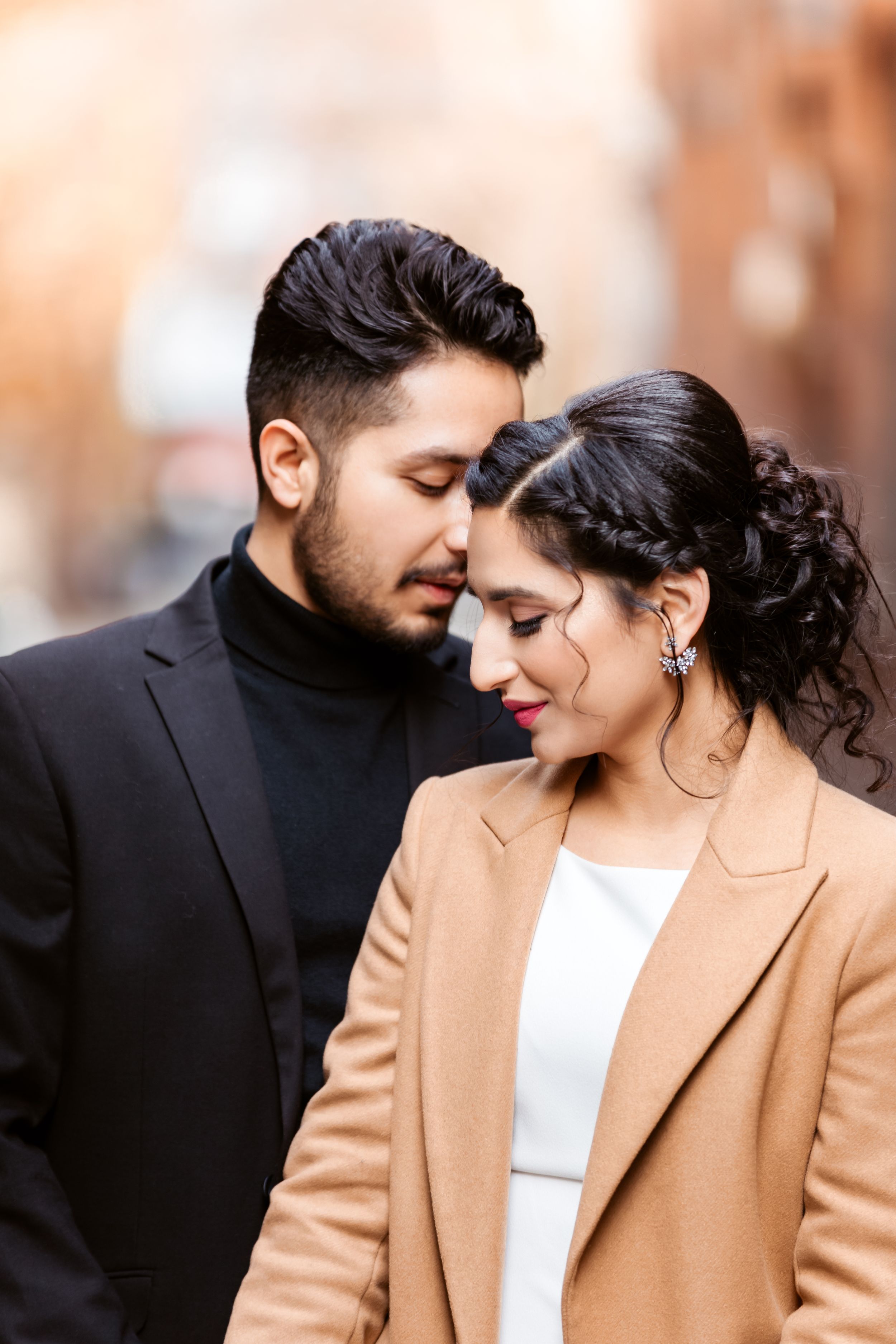 An intimate portrait of a couple in formal wear sharing a tender moment against a blurred urban backdrop.
