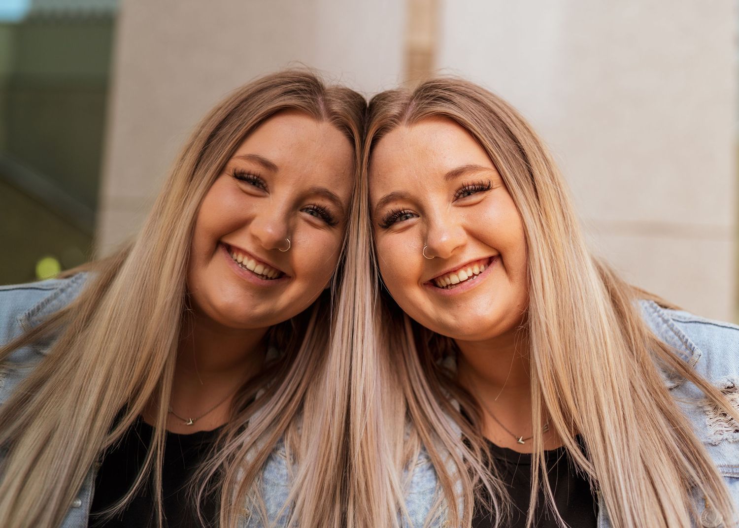 Matching portrait of two people with blonde hair smiling against light background.