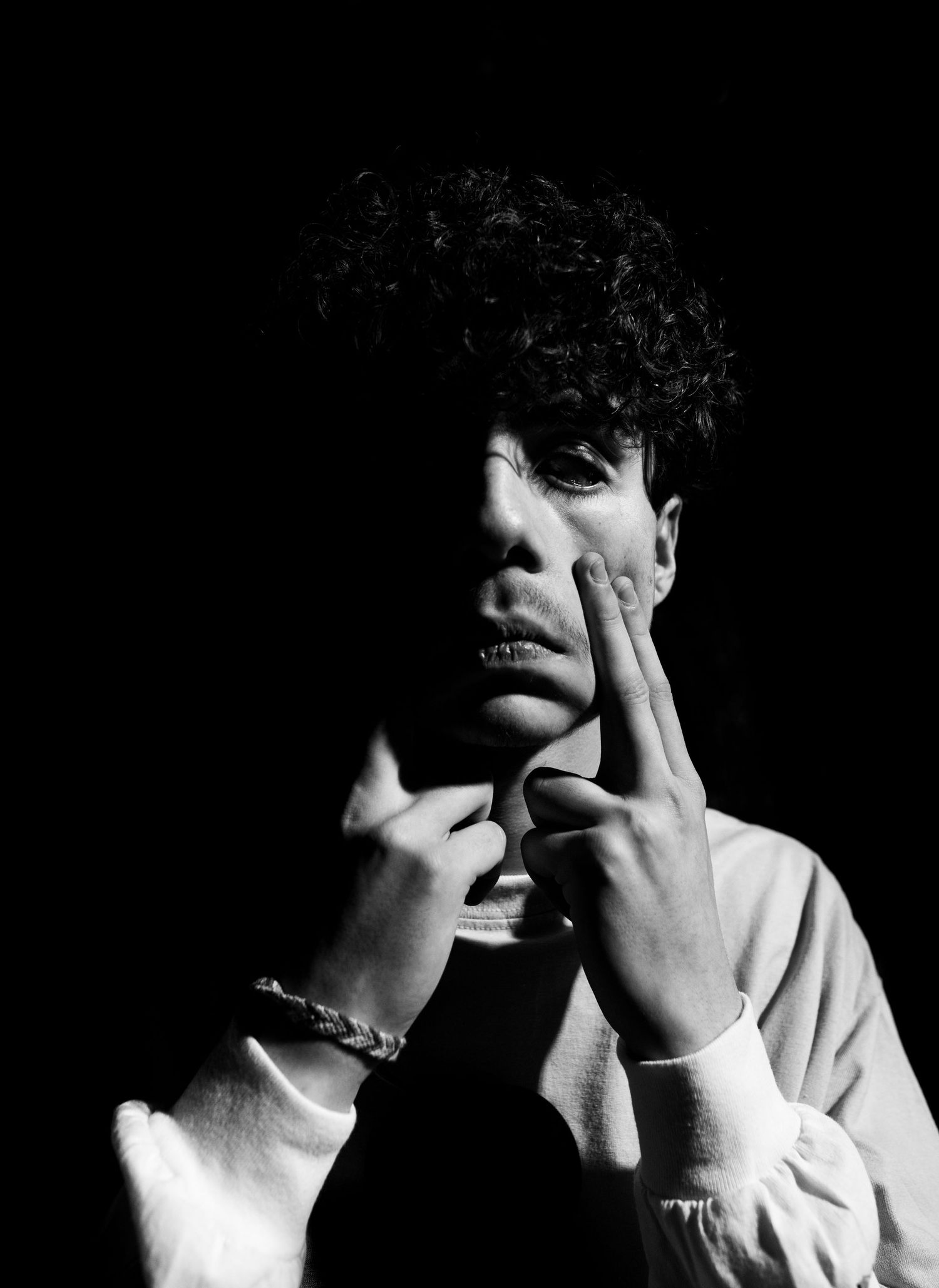 Dramatic black and white portrait showing hands touching face in moody lighting.