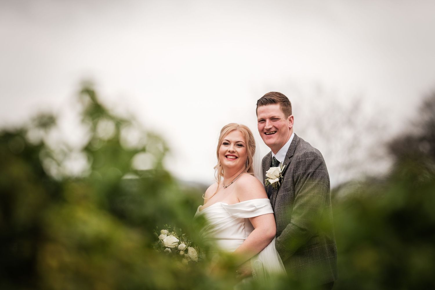 A romantic outdoor wedding portrait captured against a soft-focus natural background.