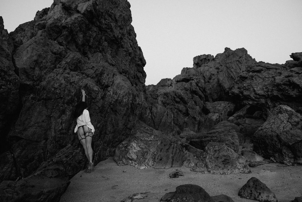 A person stands in a crevice between dramatic rocky cliffs in black and white photography.