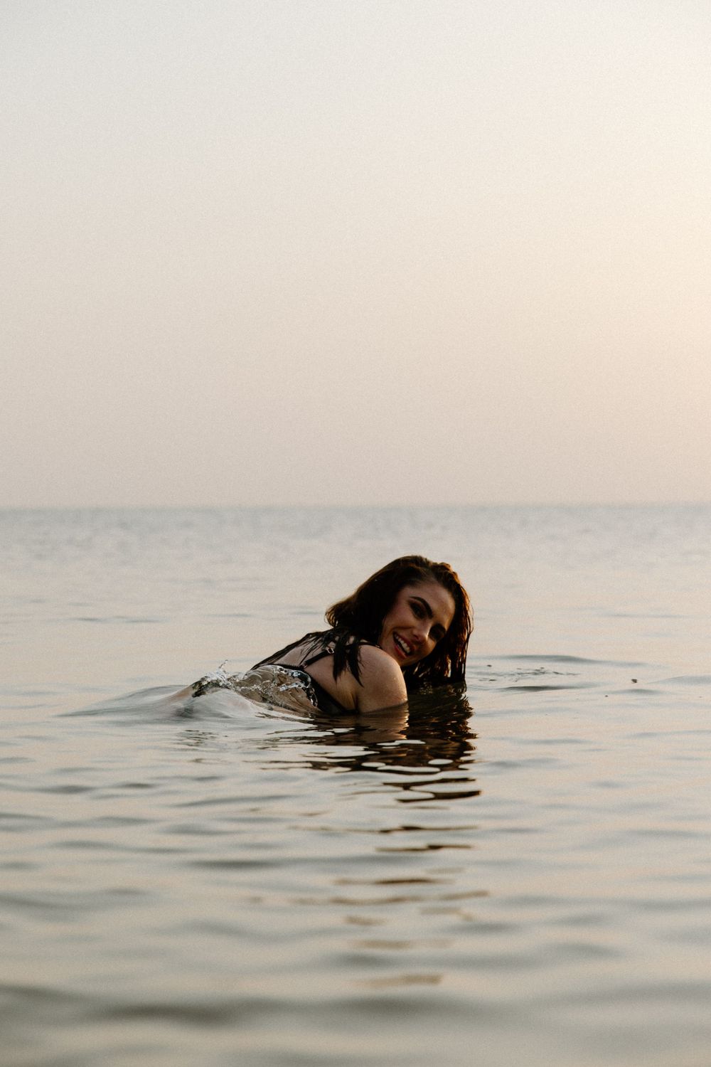 A person enjoying a swim in calm ocean waters during sunset, with their body partially submerged.