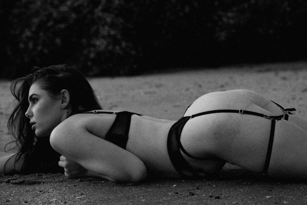Black and white boudoir photography of a model in lingerie lying on the ground in an artistic pose.