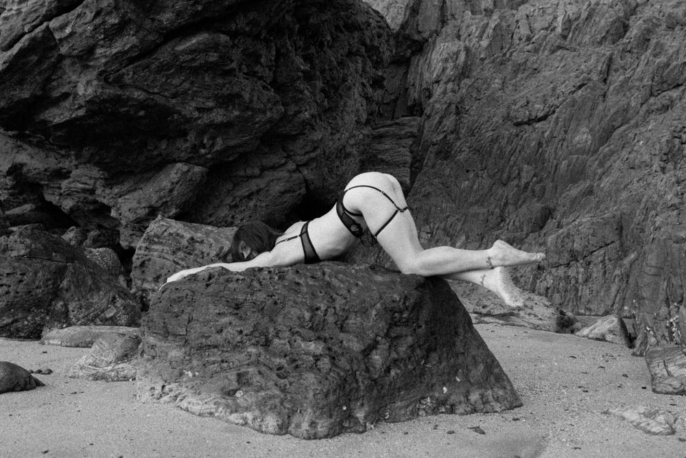 A person in a bikini gracefully poses on a rocky coastal formation in black and white photography.