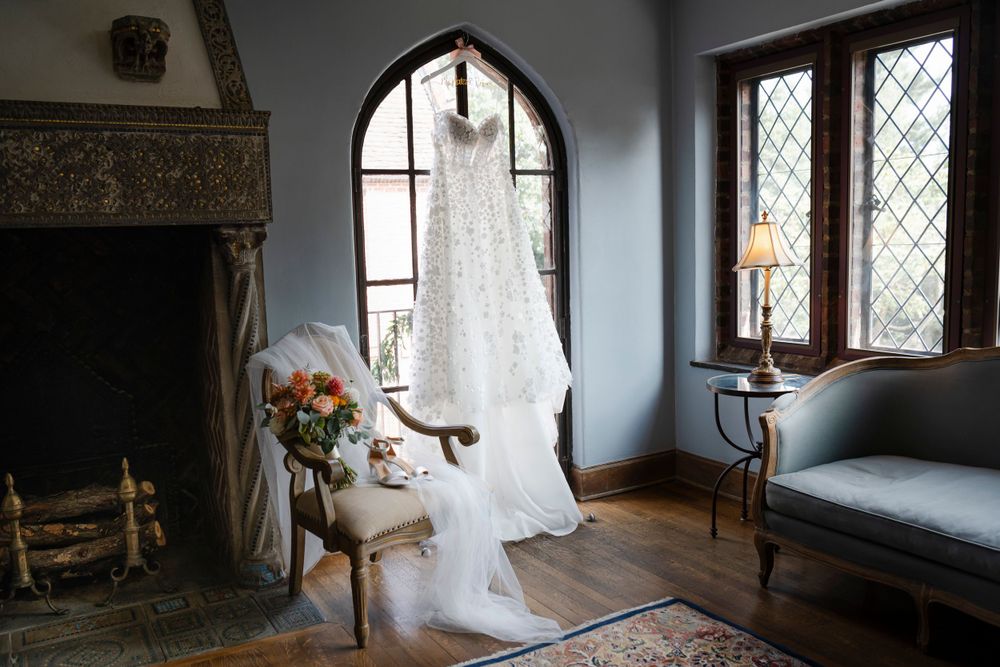 A white lace wedding dress hangs in an elegant bridal suite with gothic windows and antique furniture at Aldie Mansion.