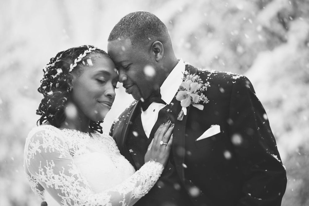Black and white romantic wedding portrait with soft snowflakes falling around a loving couple in formal attire.