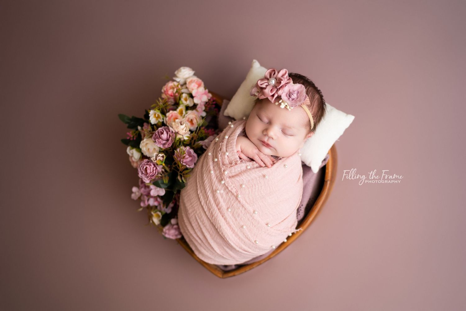 Newborn baby posed with pink flowers and soft textures in studio setting.