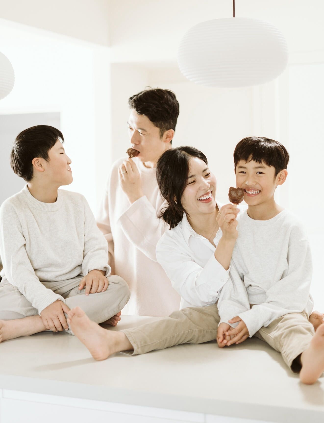 Two sons on the kitchen benchtop, with their parents feeding them ice cream in their Melbourne home.
