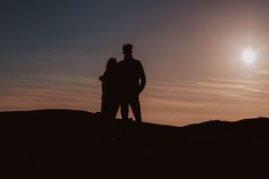 Silhouette of a young couple having a hug as the sun is setting behind them.