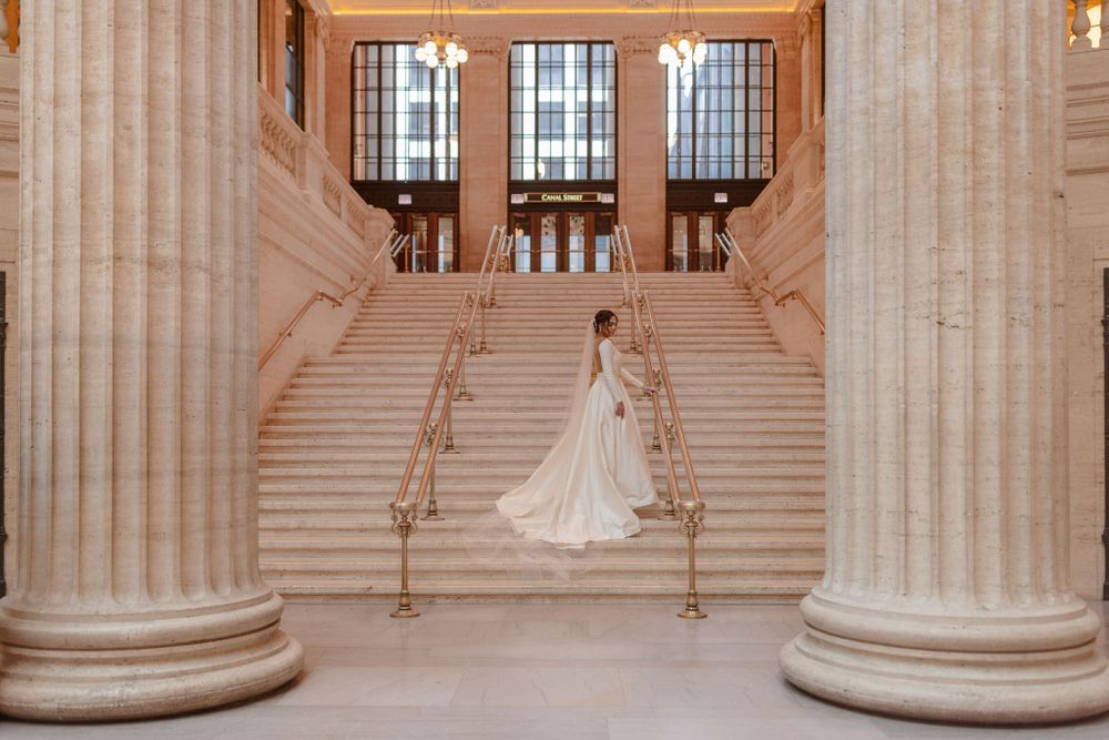 Wedding dress with long train flowing down ornate marble staircase between classical columns.