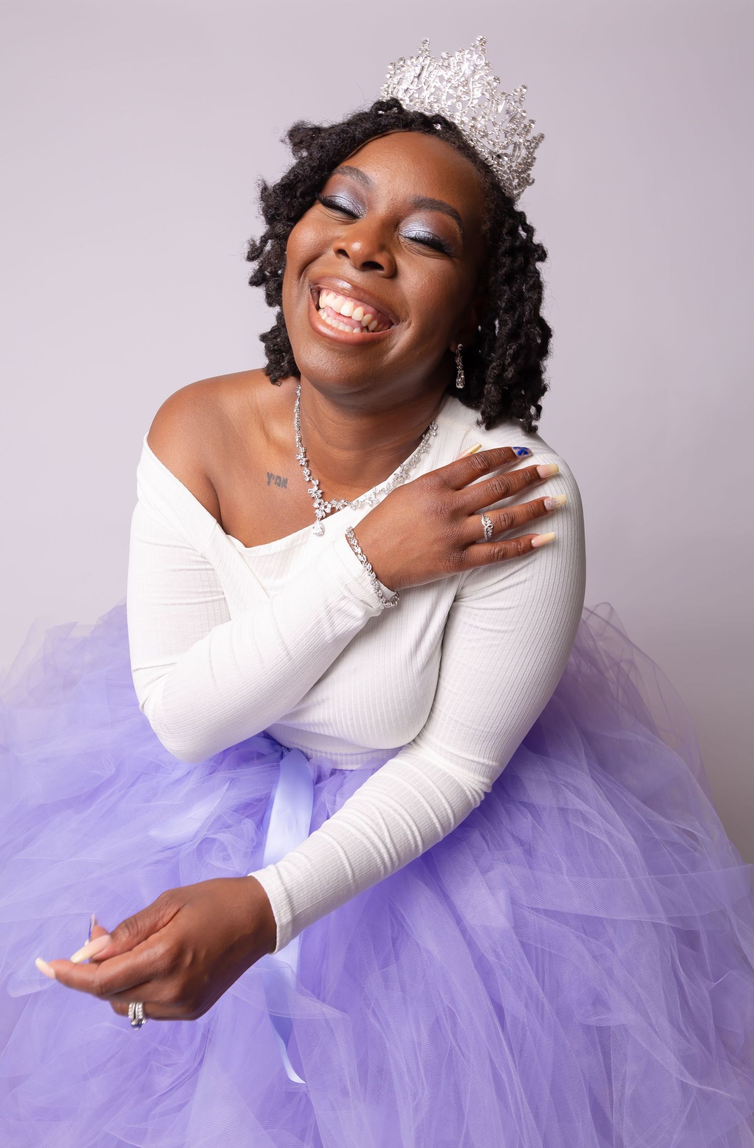 Joyful pose in white long-sleeve top and purple tulle skirt with crystal crown.