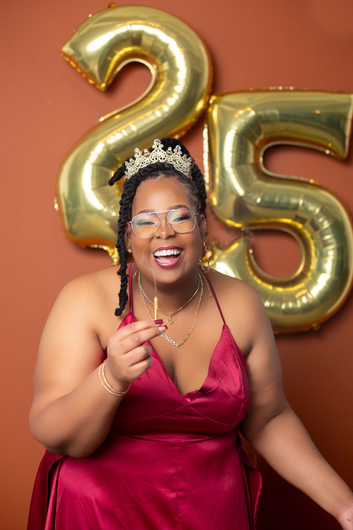 Celebratory 25th birthday scene with gold number balloons and a person in a red dress wearing a tiara.