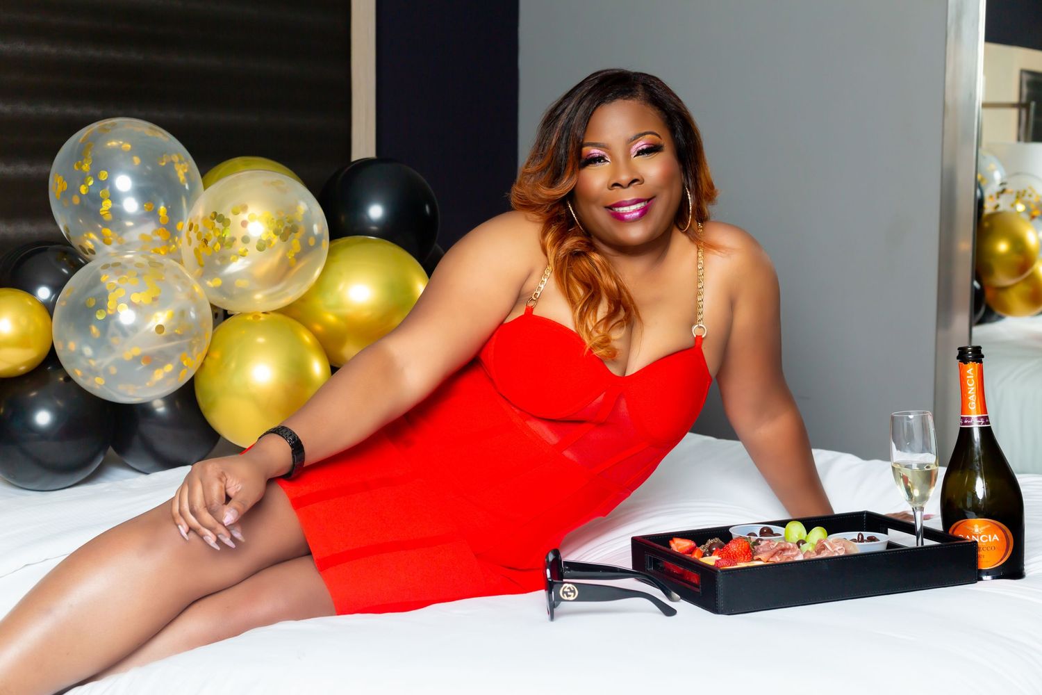 Celebratory photoshoot with champagne and appetizers featuring a red cocktail dress.