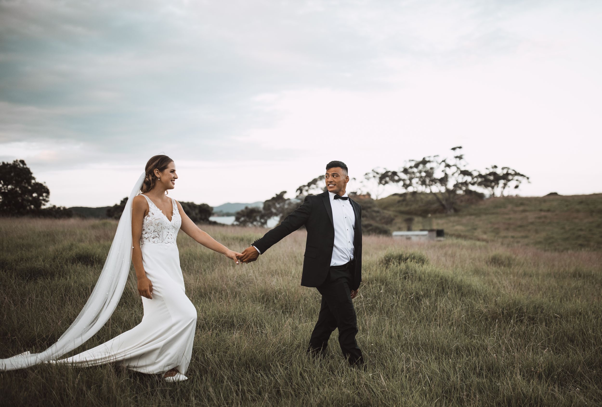 Couple dances together in a rustic field with dramatic cloudy sky.