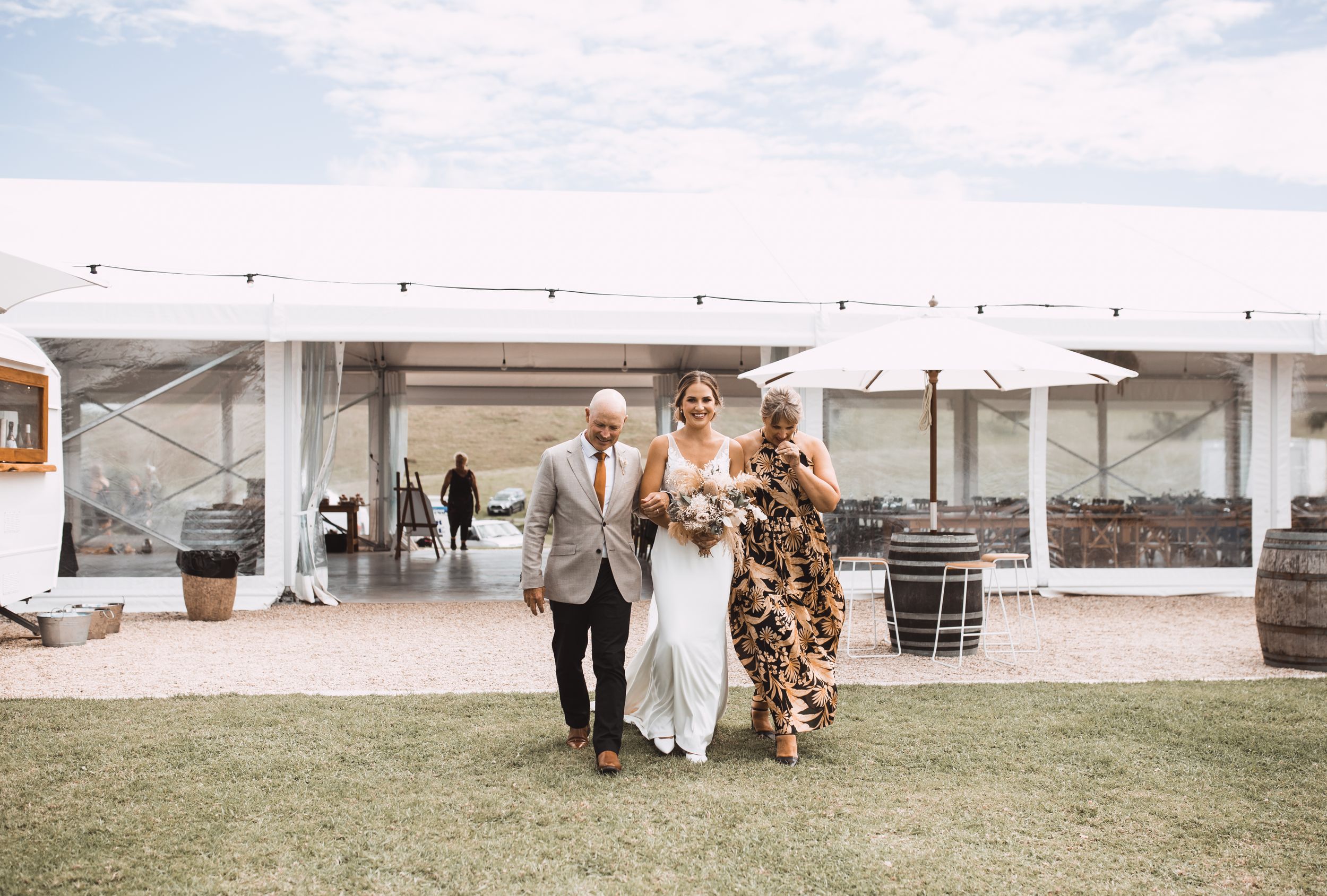 Wedding party gathered under a white tent during an outdoor celebration.