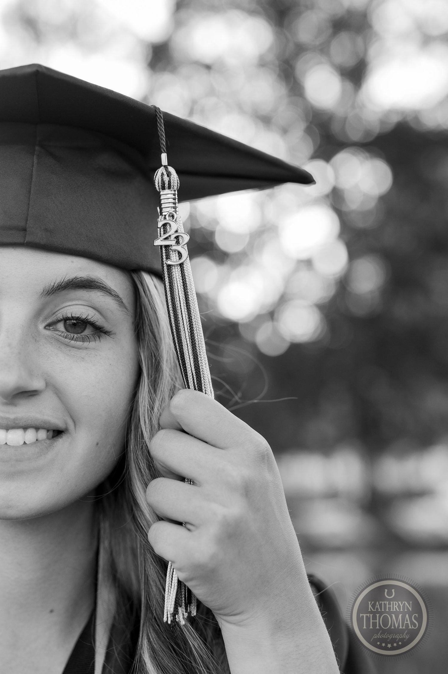 Close-up black and white portrait showing graduation cap with tassel against bokeh background.