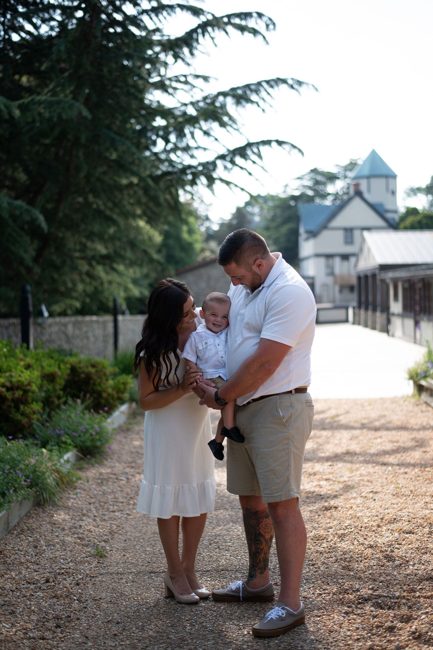 A family shares an intimate moment on a gravel path with a church visible in the background.