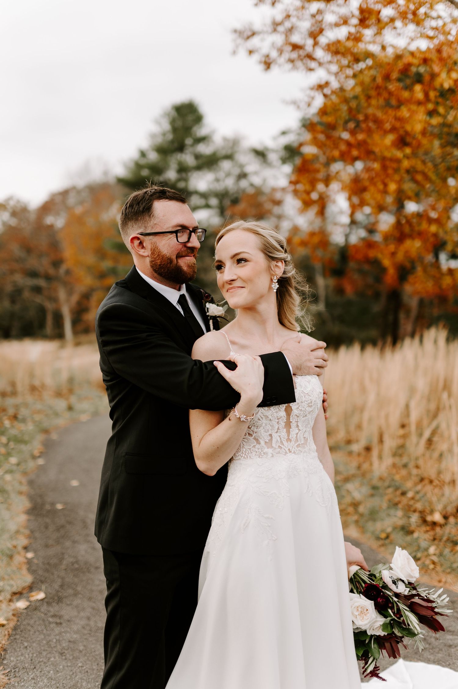 A romantic autumn wedding portrait with orange leaves and a white gown on a rustic path.
