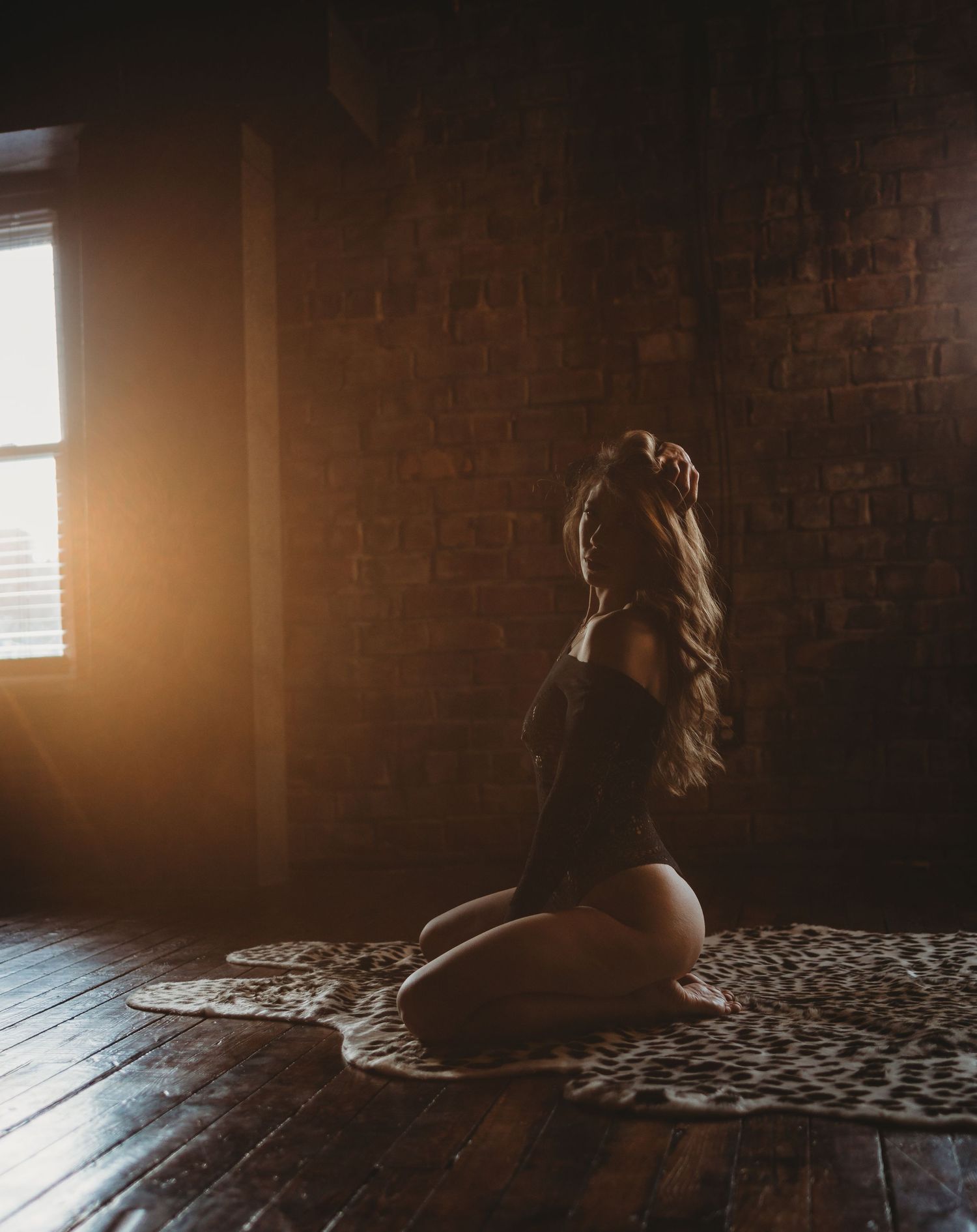 Dark moody room with sunlight streaming through window creating dramatic lighting and shadows on brick wall.